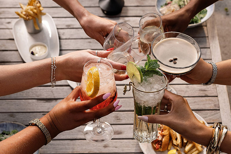 overhead view of people toasting with cocktails over a table of food